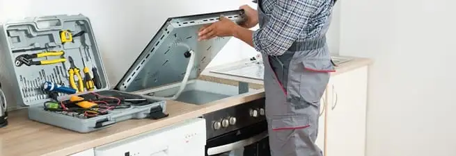 Cooktop repair technician lifting a built-in stovetop for service in Cedar Rapids, IA
