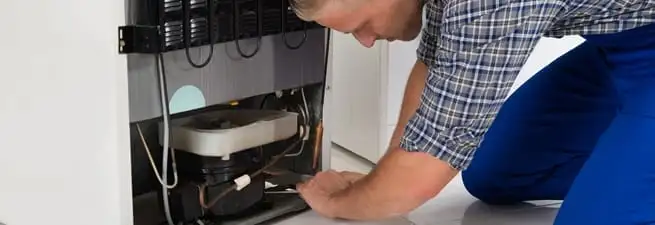Refrigerator repair technician servicing the compressor and condenser area in Cedar Rapids, IA