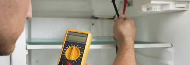 Refrigerator repair technician testing electrical components with a multimeter in Cedar Rapids, IA